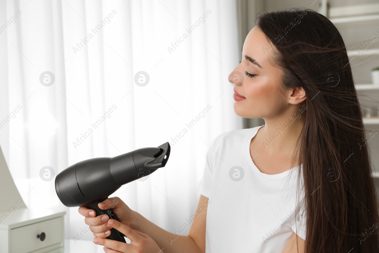 Photo of Beautiful young woman using hair dryer at home