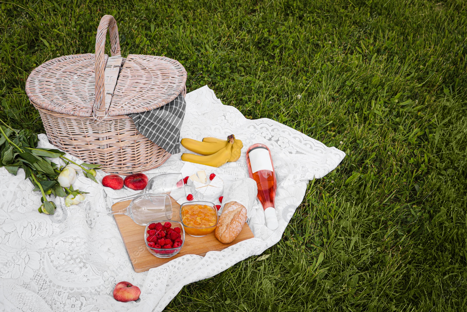 Photo of Picnic blanket with tasty food, flowers, basket and cider on green grass outdoors. Space for text