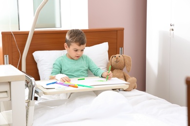 Photo of Little child with intravenous drip drawing in hospital bed