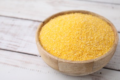 Photo of Raw cornmeal in bowl on light wooden table, closeup. Space for text