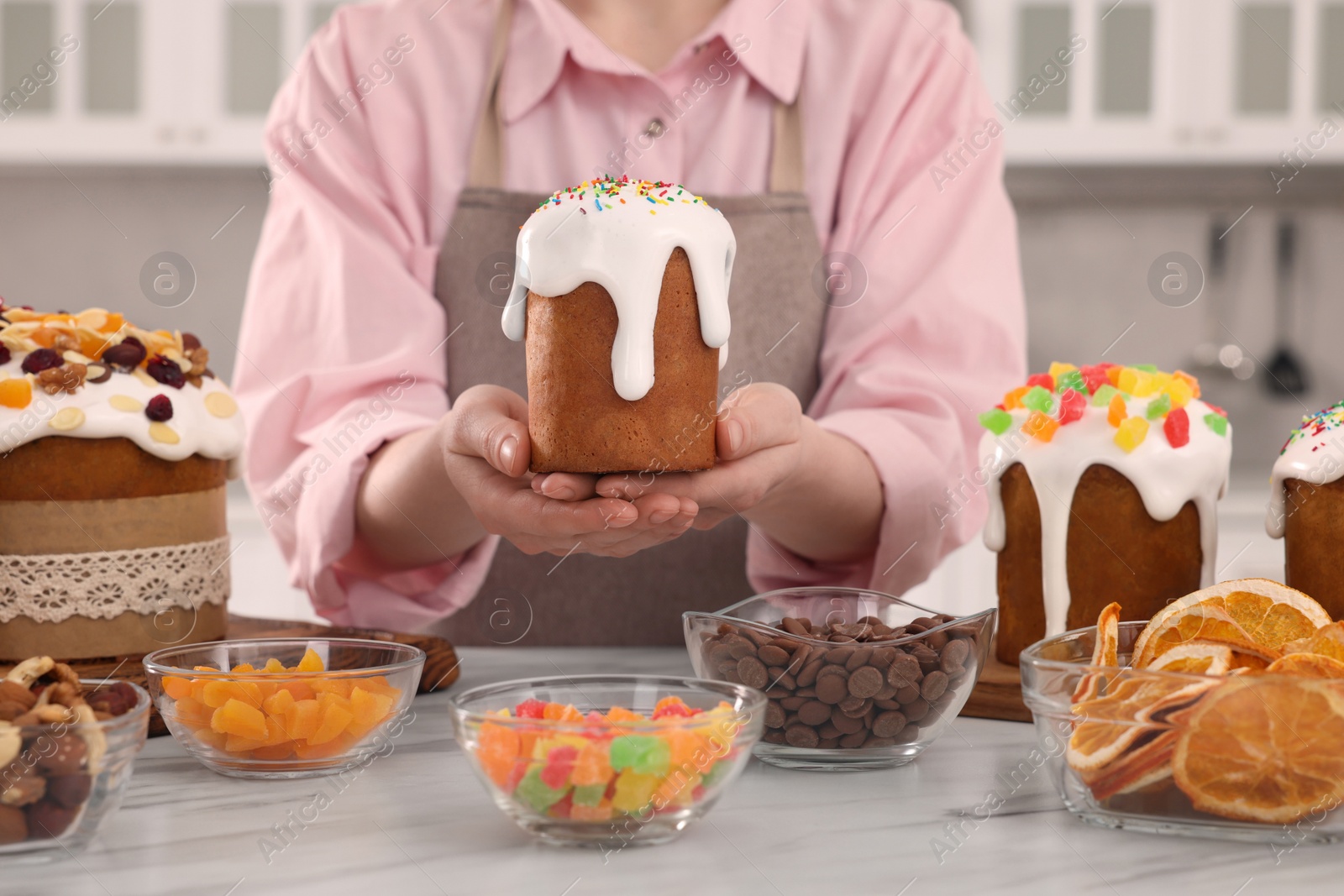 Photo of Woman holding delicious Easter cake with sprinkles at white marble table in kitchen, closeup