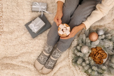 Photo of Young woman with cocoa and cookies sitting on light blanket, top view. Christmas holiday