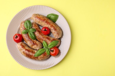 Photo of Plate with tasty homemade sausages, basil leaves and tomatoes on yellow table, top view. Space for text