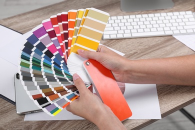 Photo of Woman with color palette samples at table, closeup