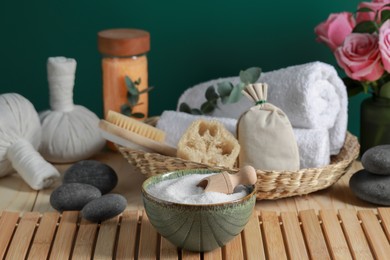Photo of Beautiful composition with sea salt, flowers and different spa products on wooden table near green wall