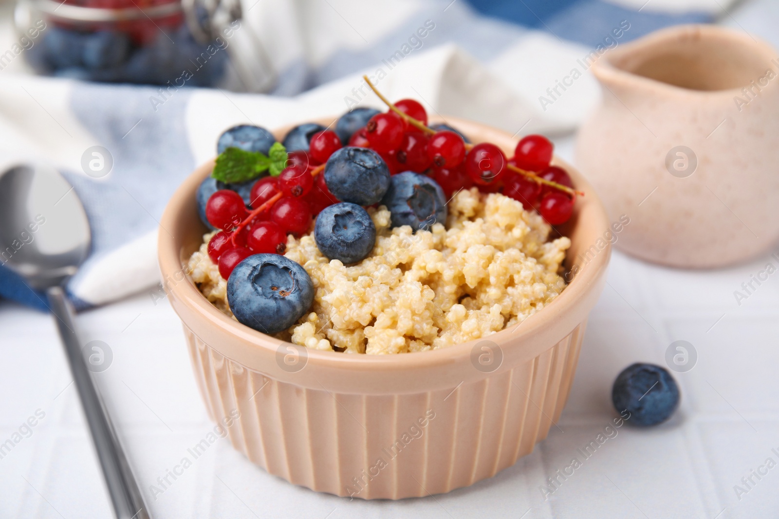 Photo of Bowl of delicious cooked quinoa with blueberries and cranberries on white tiled table, closeup