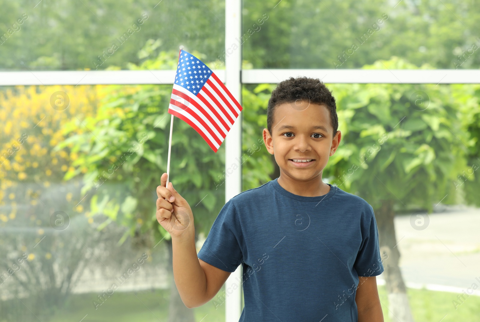 Photo of Happy African-American boy holding national flag near window indoors