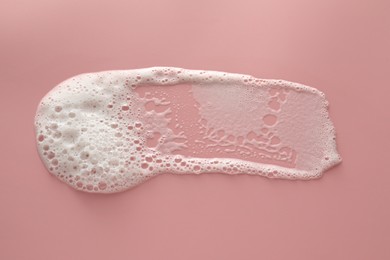Photo of Smudge of white washing foam on pale pink background, top view