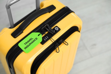 Above view of yellow suitcase with TRAVEL INSURANCE label indoors, closeup