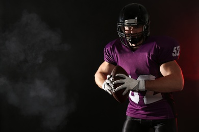 Photo of American football player with ball on dark background. Space for text