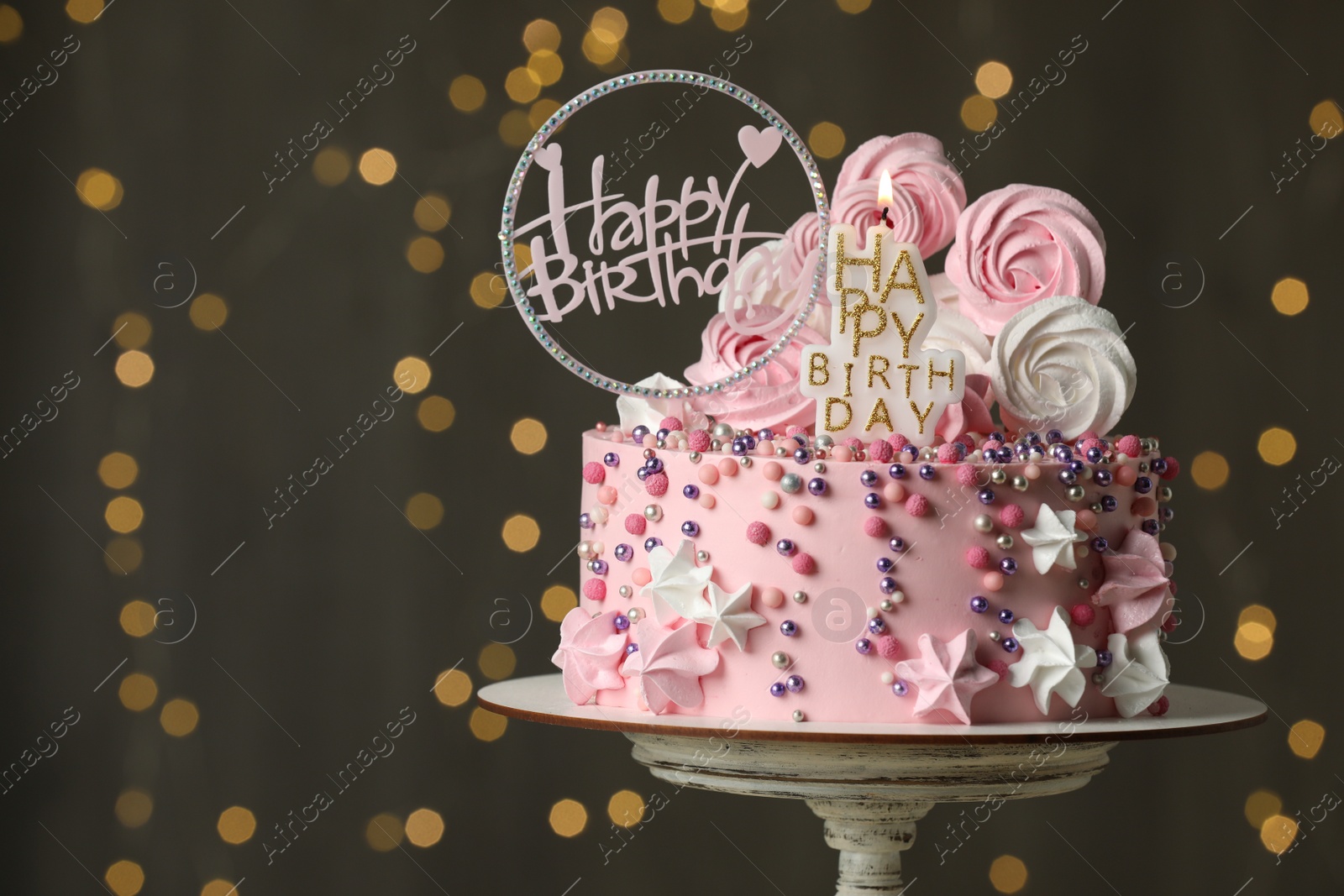 Photo of Beautiful birthday cake with decor on stand against festive lights. Space for text