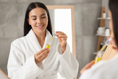 Photo of Young woman with cosmetic serum in her hands in bathroom
