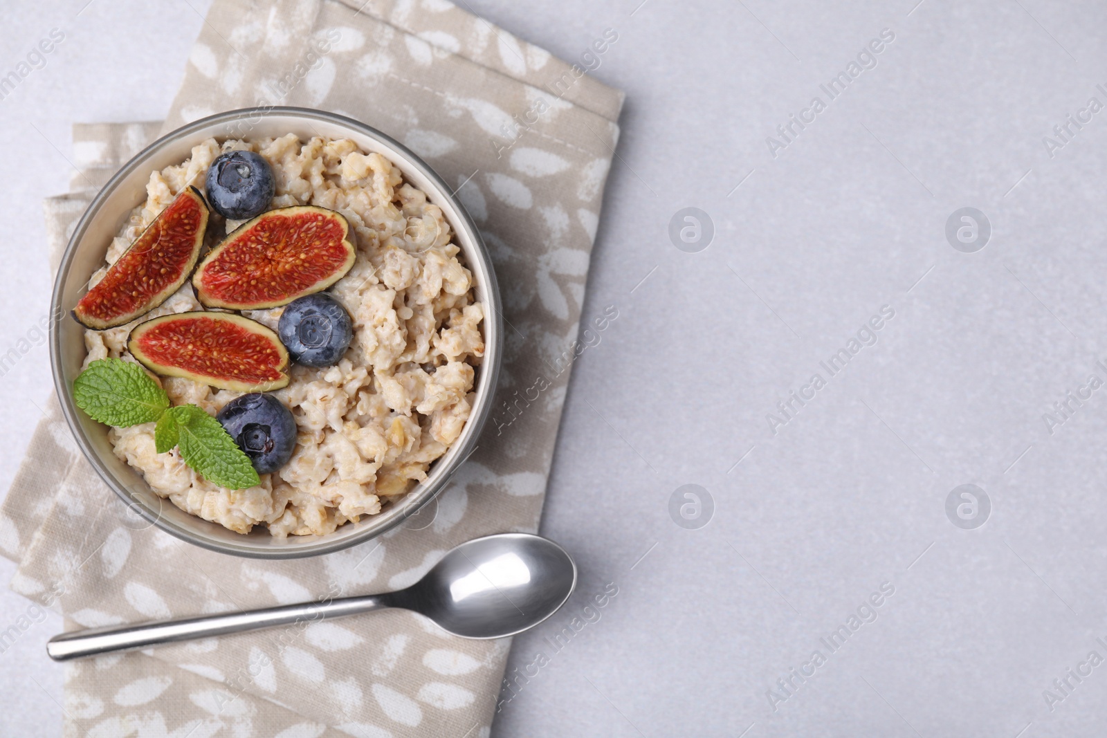 Photo of Oatmeal served with blueberries, mint and fig pieces on light grey table, top view. Space for text