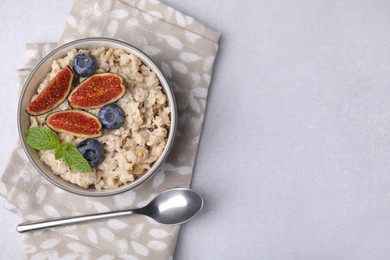 Oatmeal served with blueberries, mint and fig pieces on light grey table, top view. Space for text