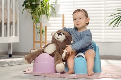 Photo of Little child and teddy bear sitting on plastic baby potties indoors