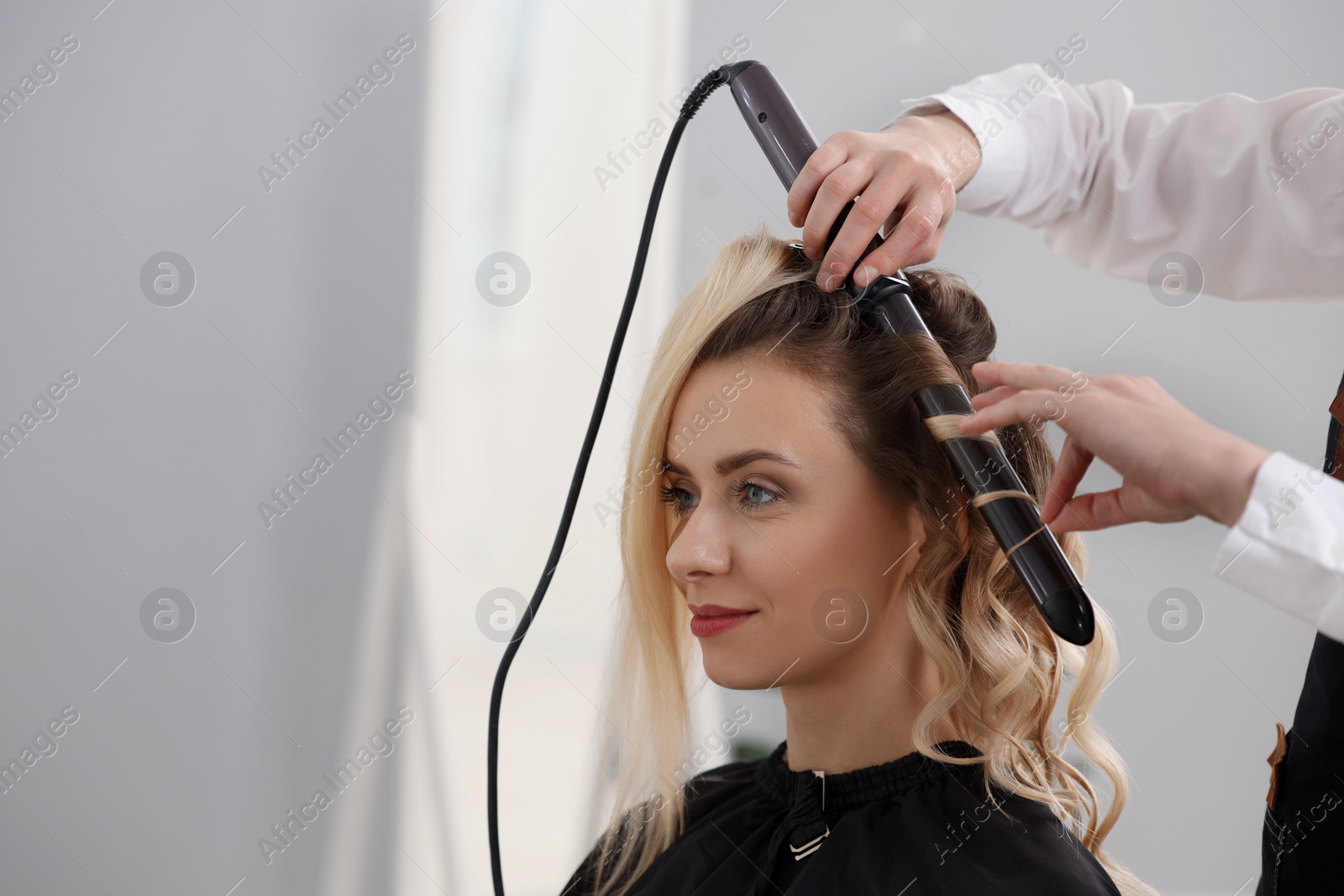 Photo of Hair styling. Hairdresser curling woman's hair in salon, closeup. Space for text