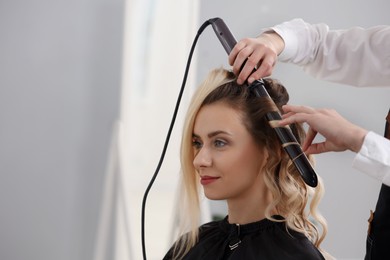 Photo of Hair styling. Hairdresser curling woman's hair in salon, closeup. Space for text