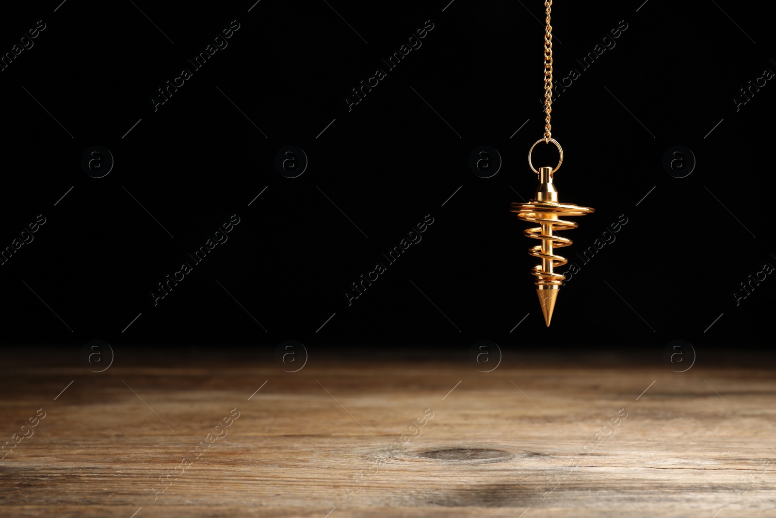 Photo of Stylish pendulum above wooden table on black background, space for text. Hypnotherapy session