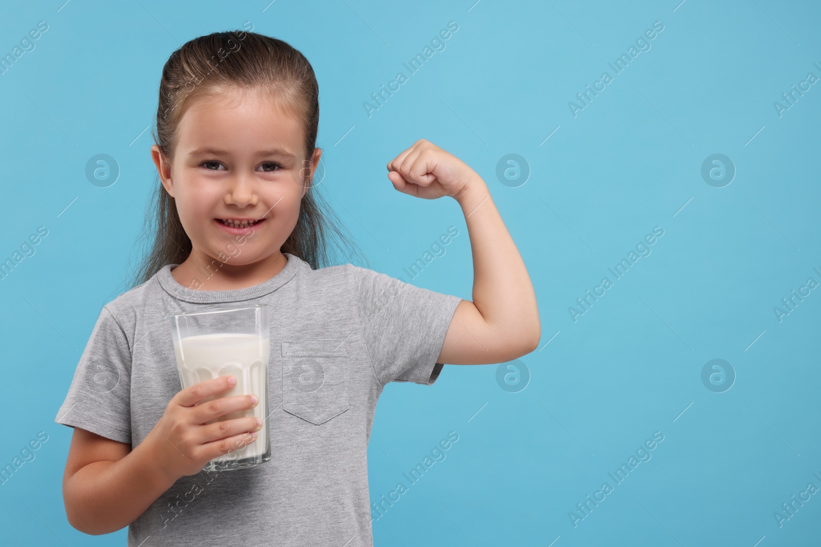 Photo of Cute girl with glass of fresh milk showing her strength on light blue background, space for text