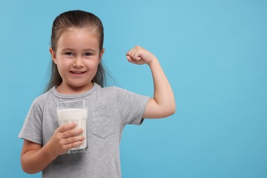 Photo of Cute girl with glassfresh milk showing her strength on light blue background, space for text