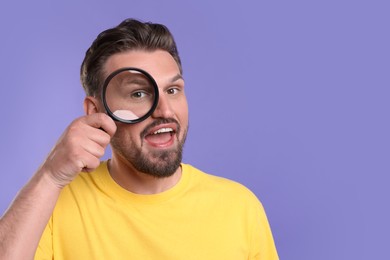 Photo of Emotional man looking through magnifier on violet background. Space for text