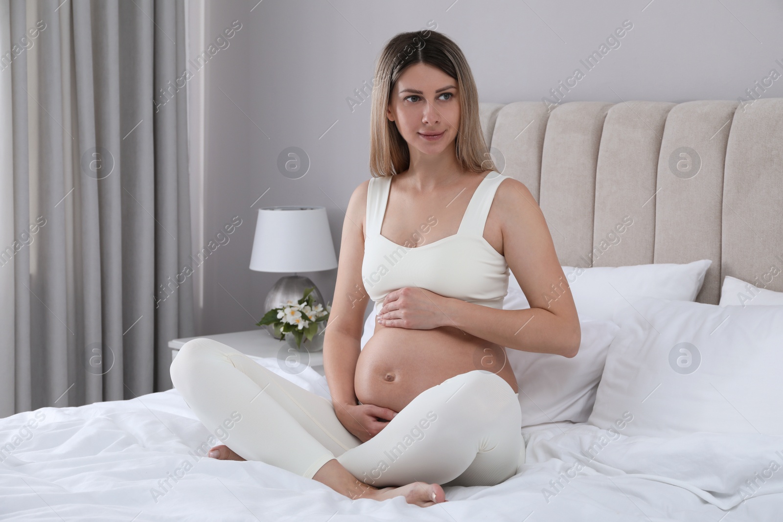 Photo of Beautiful pregnant woman sitting on bed at home
