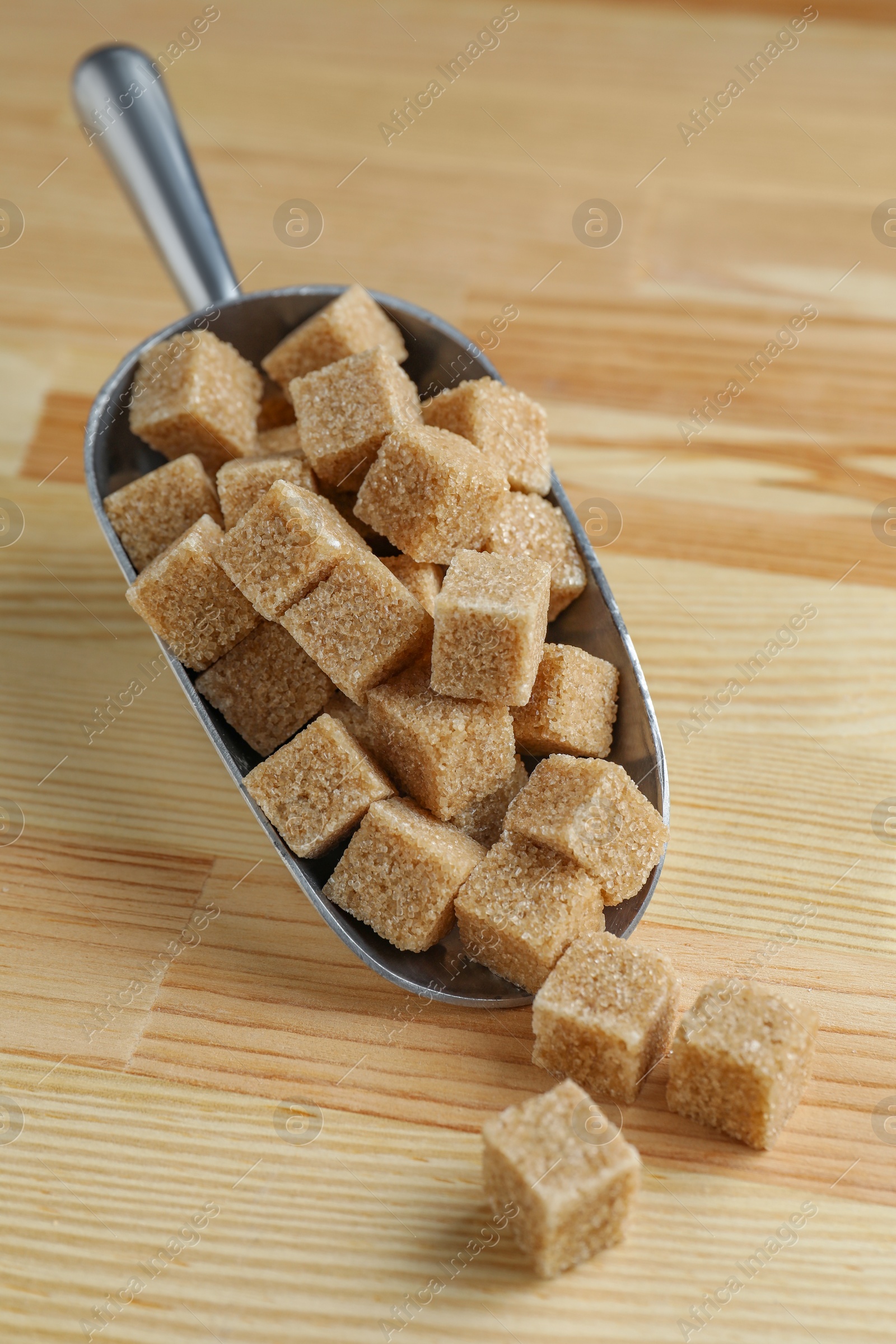 Photo of Brown sugar cubes in scoop on wooden table, closeup