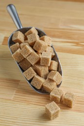 Photo of Brown sugar cubes in scoop on wooden table, closeup