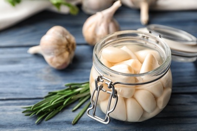 Preserved garlic in glass jar on wooden table, closeup. Space for text