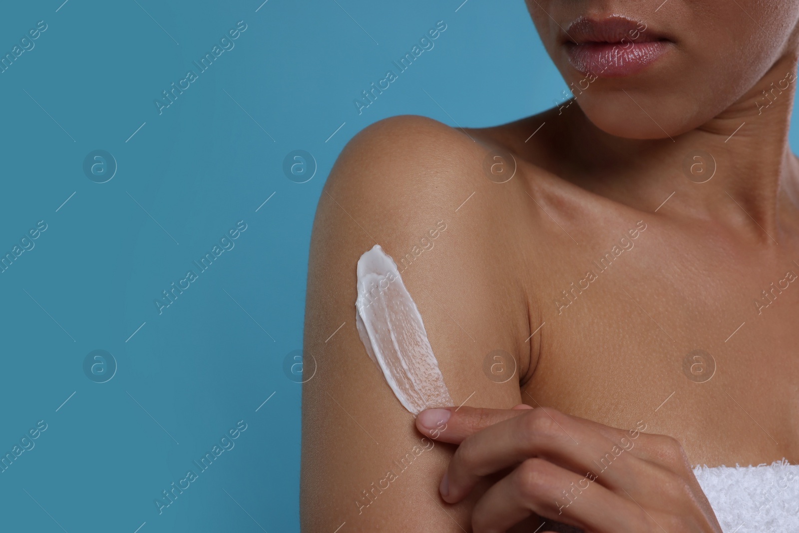 Photo of Young woman applying body cream onto arm on light blue background, closeup. Space for text