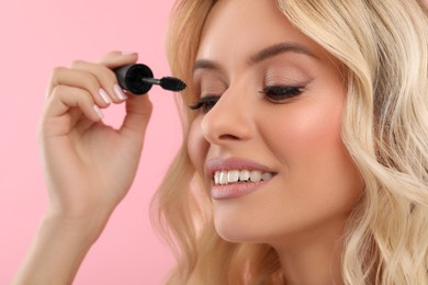 Photo of Beautiful makeup. Smiling woman applying mascara on pink background, closeup