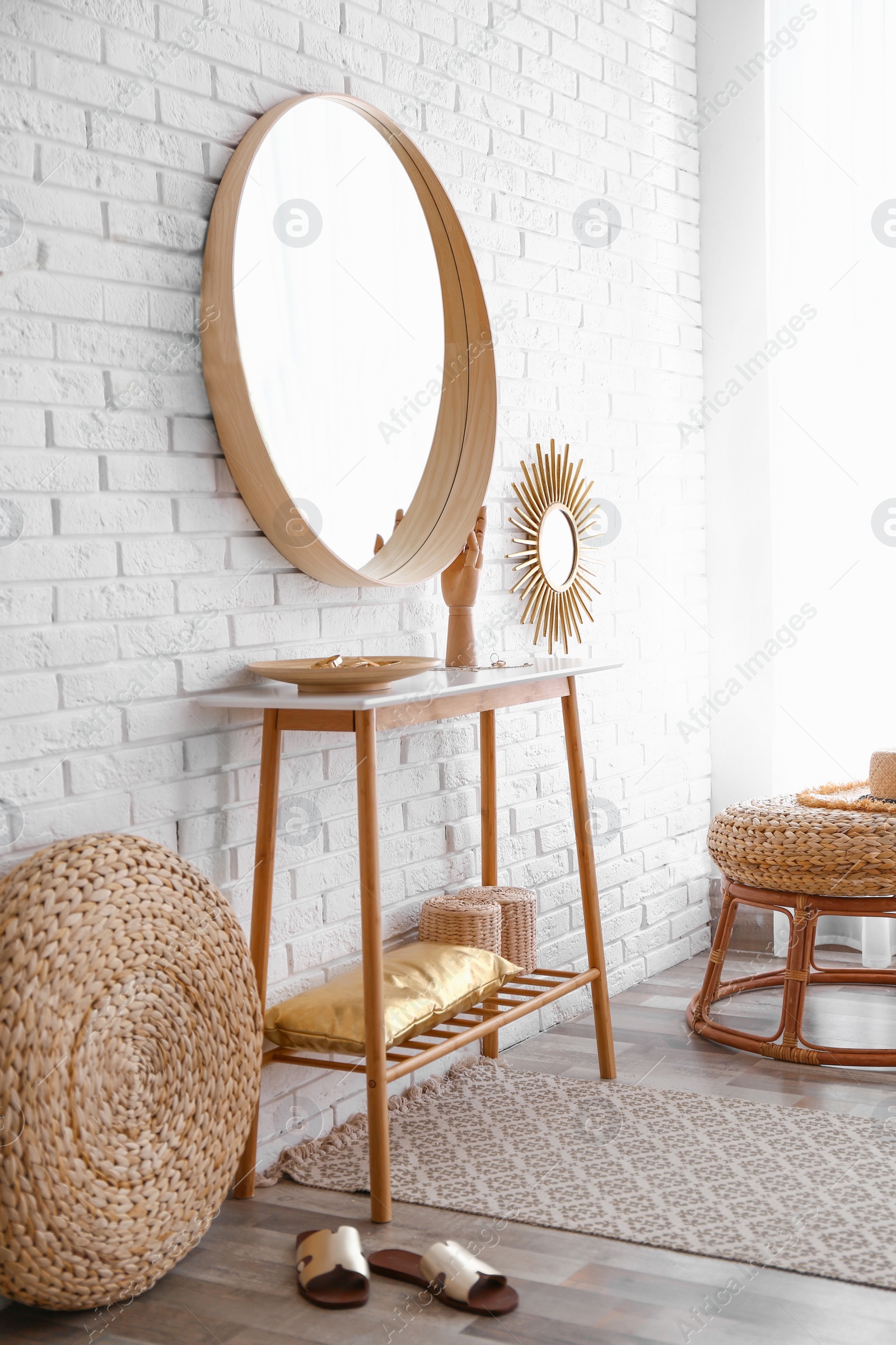 Photo of Hallway interior with big round mirror, table and decor near brick wall