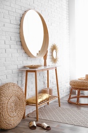 Hallway interior with big round mirror, table and decor near brick wall