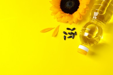 Photo of Bottle of cooking oil, sunflower and seeds on yellow background, flat lay. Space for text