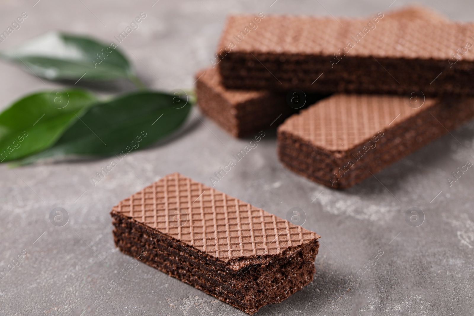 Photo of Delicious chocolate wafers with leaves on grey stone background