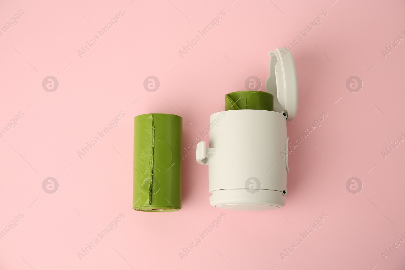 Photo of Dog waste bags and dispenser on pink background, flat lay