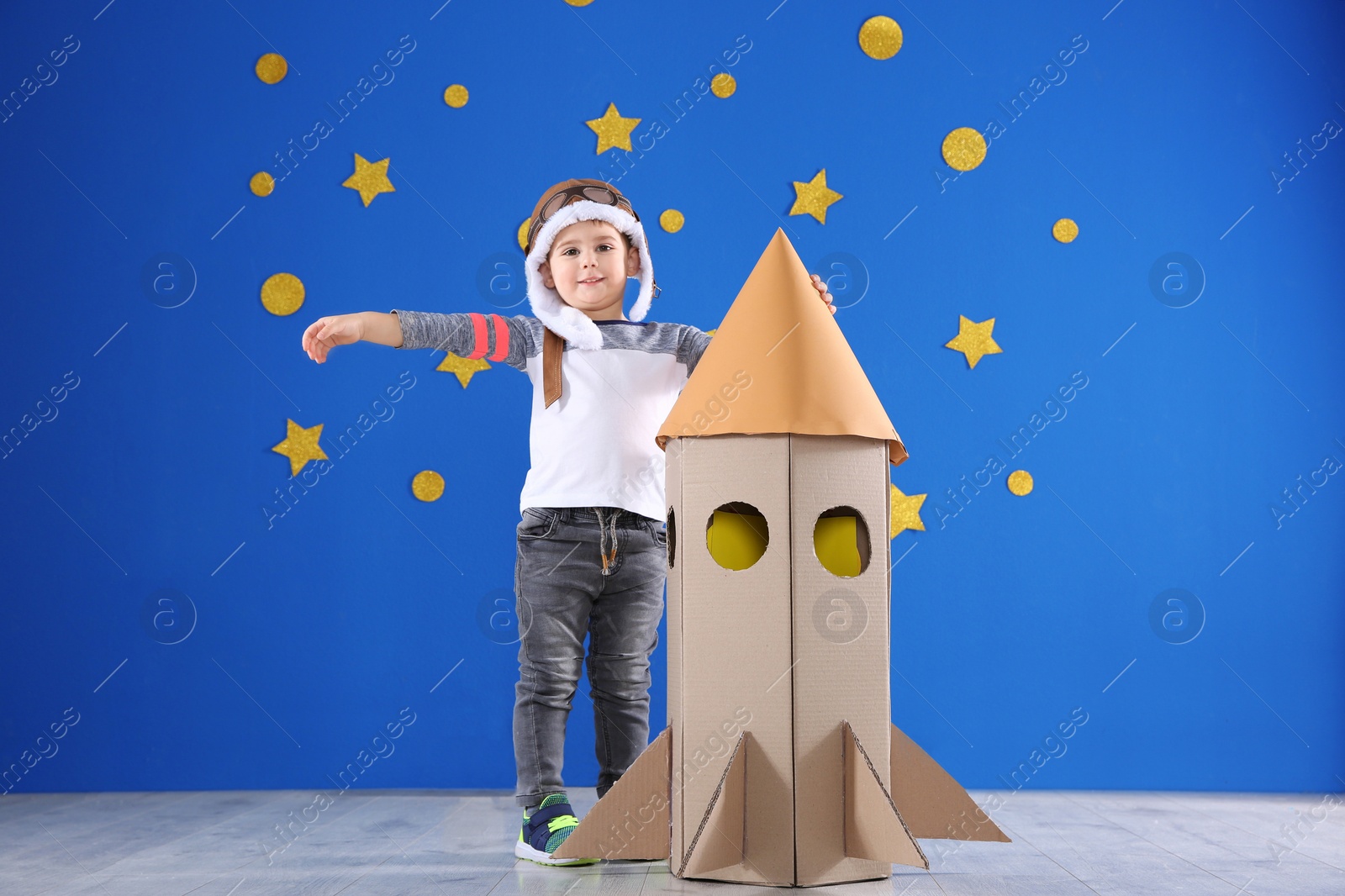 Photo of Cute little child playing with cardboard rocket near blue wall