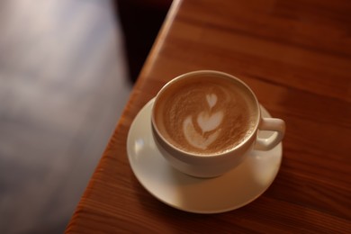 Photo of Cup of aromatic coffee with foam on wooden table in  cafe