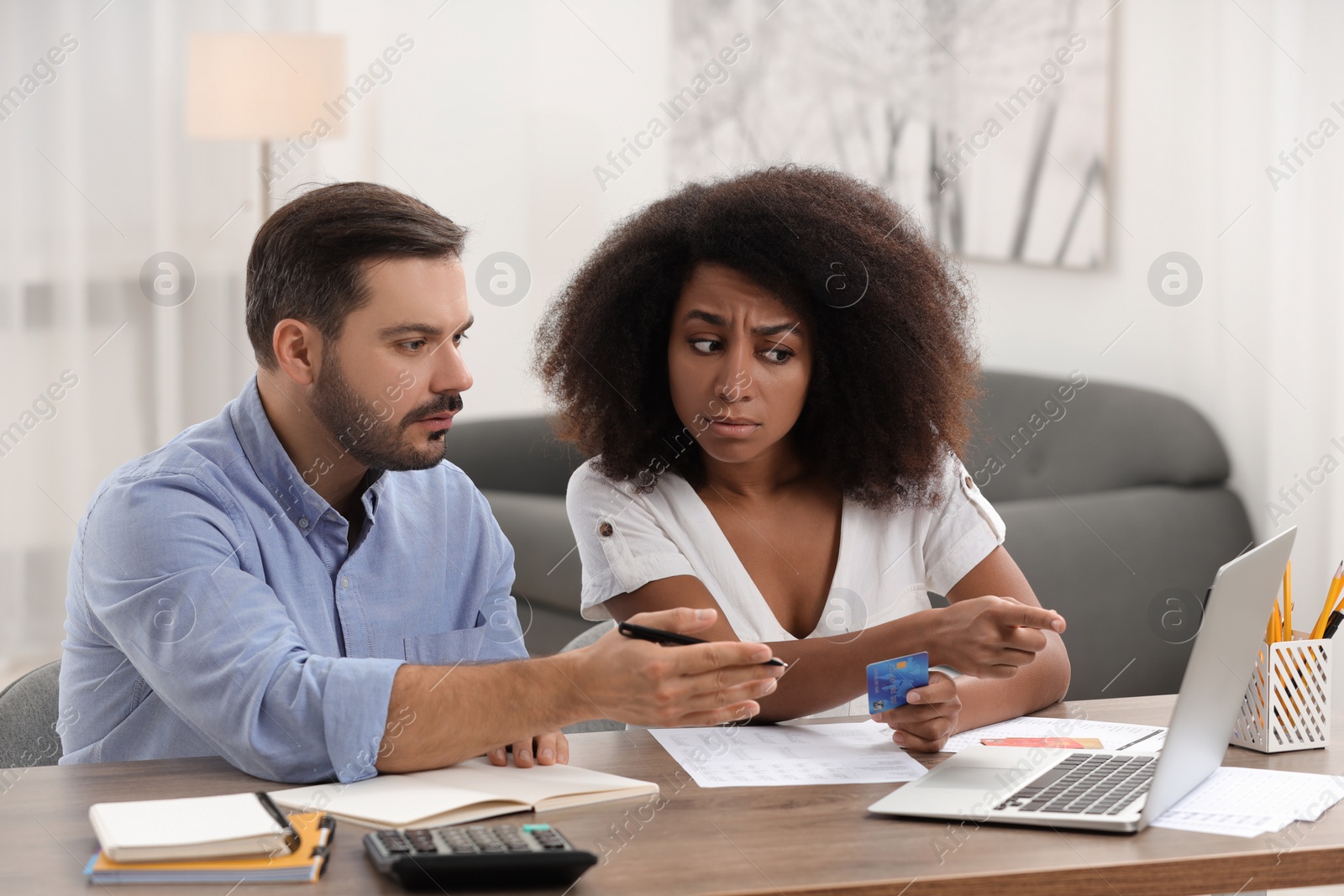 Photo of Confused couple with credit card using laptop for planning budget at home. Debt problem