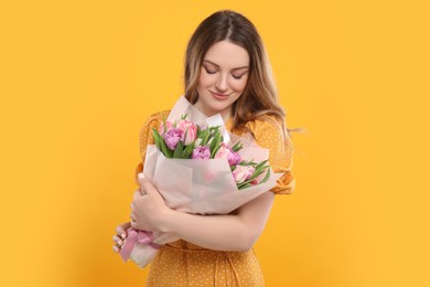 Happy young woman with bouquet of beautiful tulips on yellow background