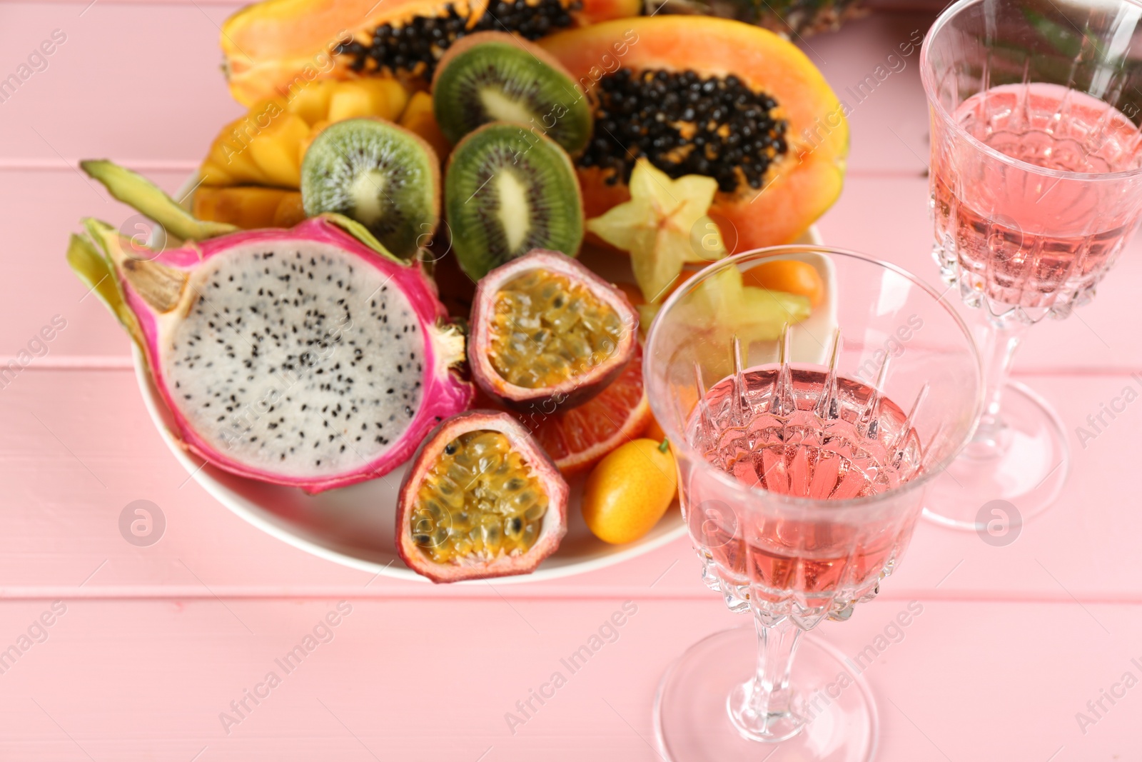 Photo of Delicious exotic fruits and wine on pink wooden table