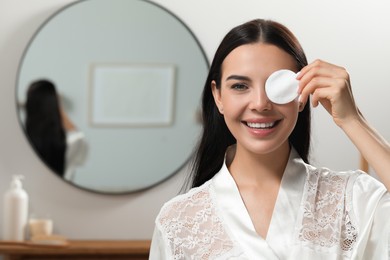 Young woman using cotton pad with micellar water indoors, space for text