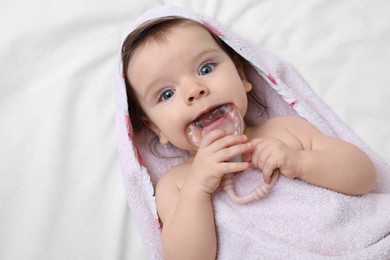 Photo of Cute little baby in hooded towel after bathing nibbling teether on bed, top view