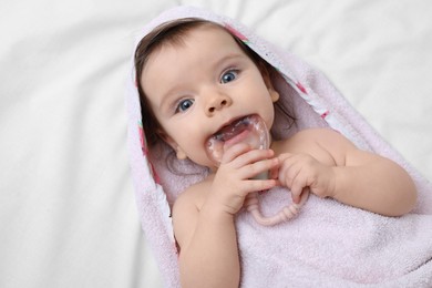 Cute little baby in hooded towel after bathing nibbling teether on bed, top view