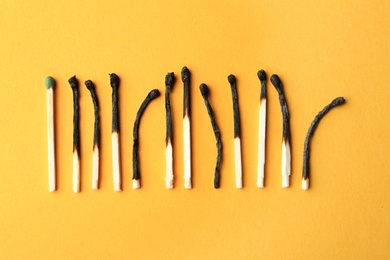Photo of Row of burnt matches and whole one on color background, flat lay. Uniqueness concept