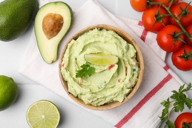 Photo of Bowl of delicious guacamole and ingredients on white tiled table, flat lay