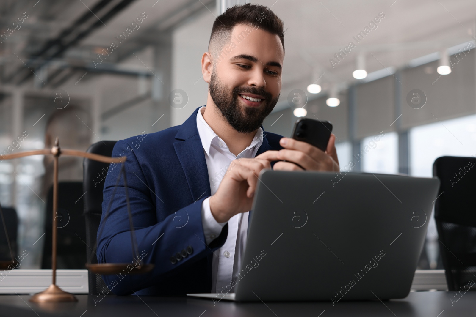 Photo of Smiling lawyer with smartphone near laptop at table in office