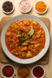 Photo of Delicious chicken curry and spices on wooden table, flat lay