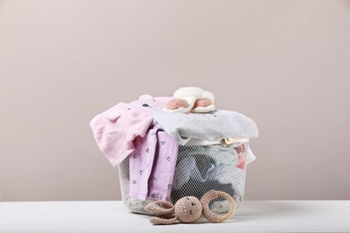 Laundry basket with baby clothes and toy on white wooden table