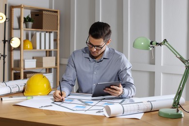 Architect working with construction drawings and tablet in office